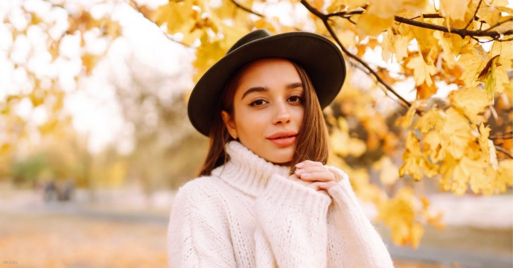 Woman in sweater and hat posing in front of a tree with yellow leaves (model)